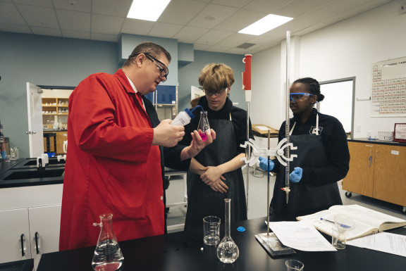 A science teacher working with two students in the lab